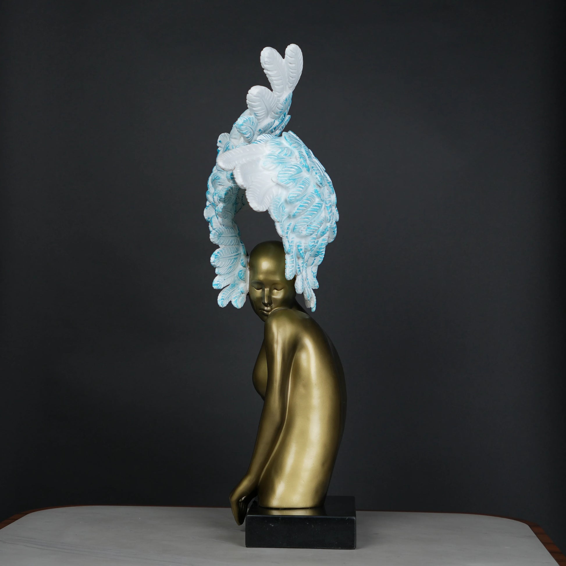 Gold-bodied woman sculpture with large white and blue feathered wings on a black base — luxury artistic décor piece.