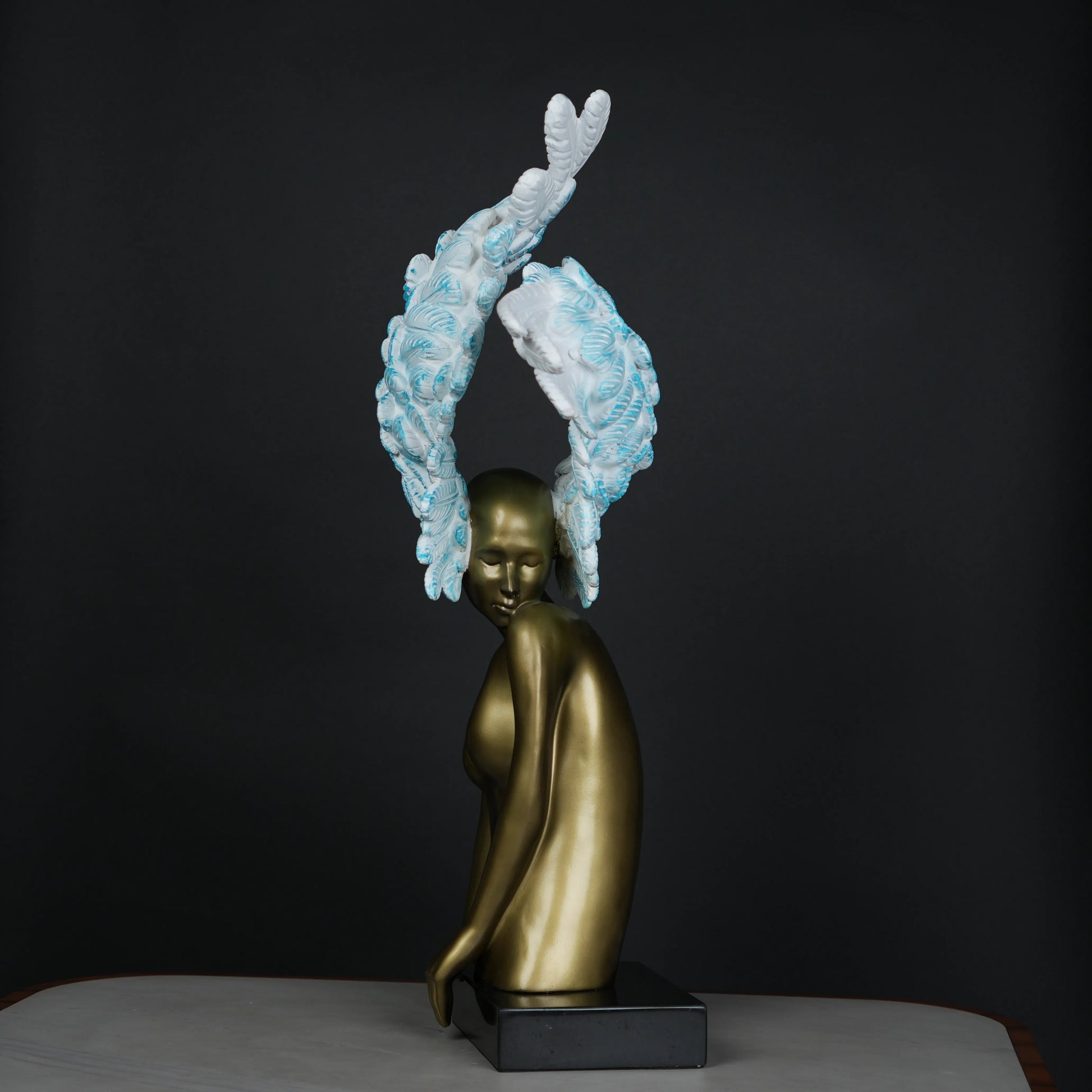 Gold-bodied woman sculpture with large white and blue feathered wings on a black base — luxury artistic décor piece.