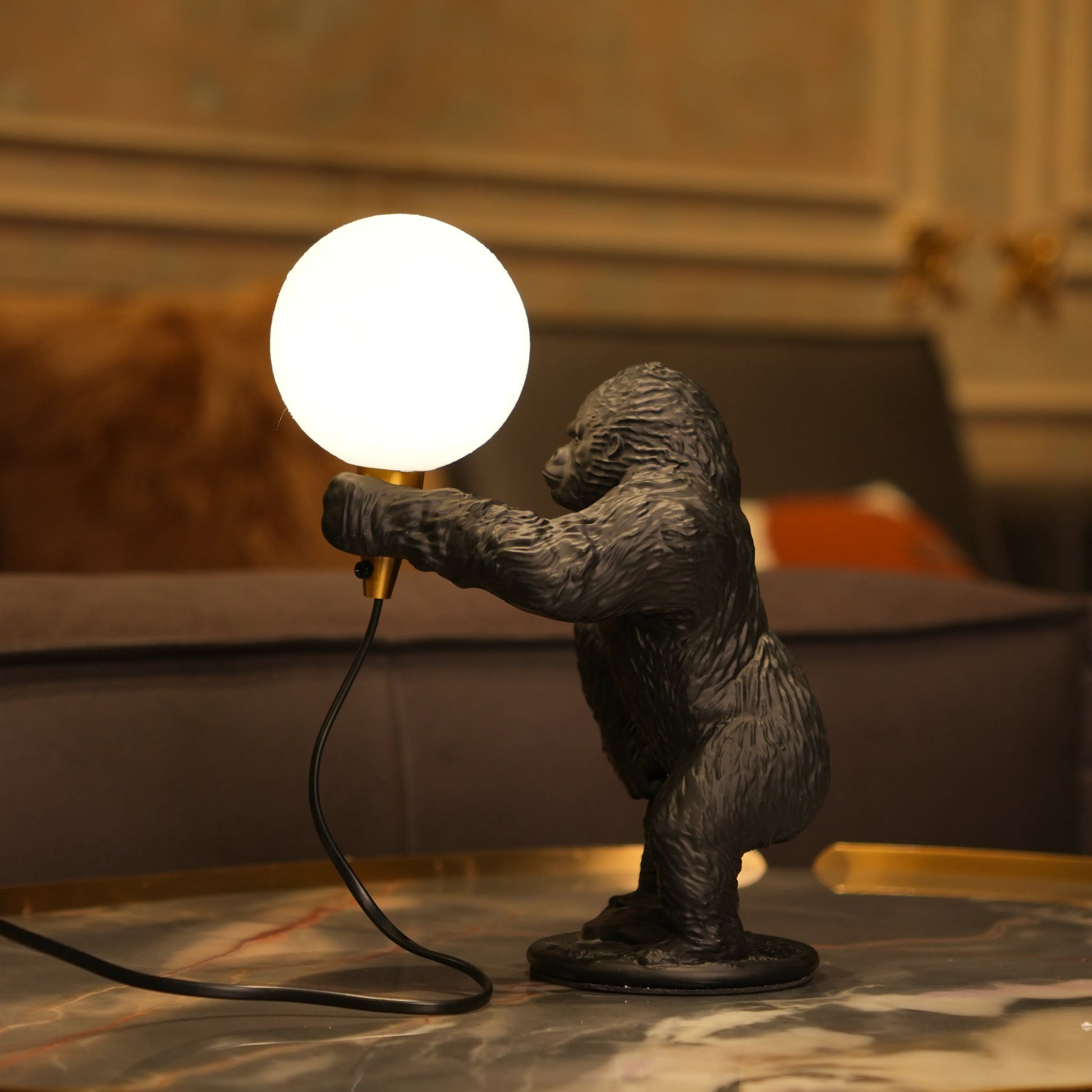 Black gorilla sculpture lamp holding a warm glowing orb with a gold lamp holder on a round black base.