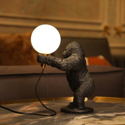 Black gorilla sculpture lamp holding a warm glowing orb with a gold lamp holder on a round black base.