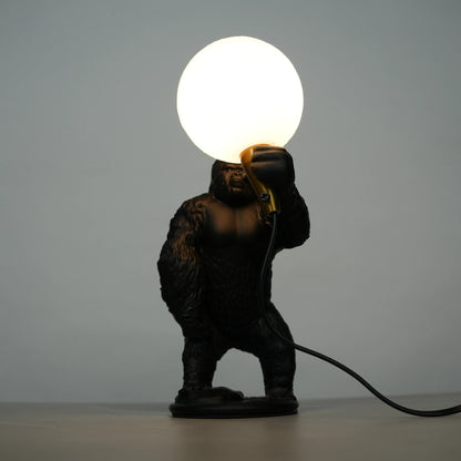 Black gorilla sculpture lamp holding a warm glowing orb with a gold lamp holder on a round black base.