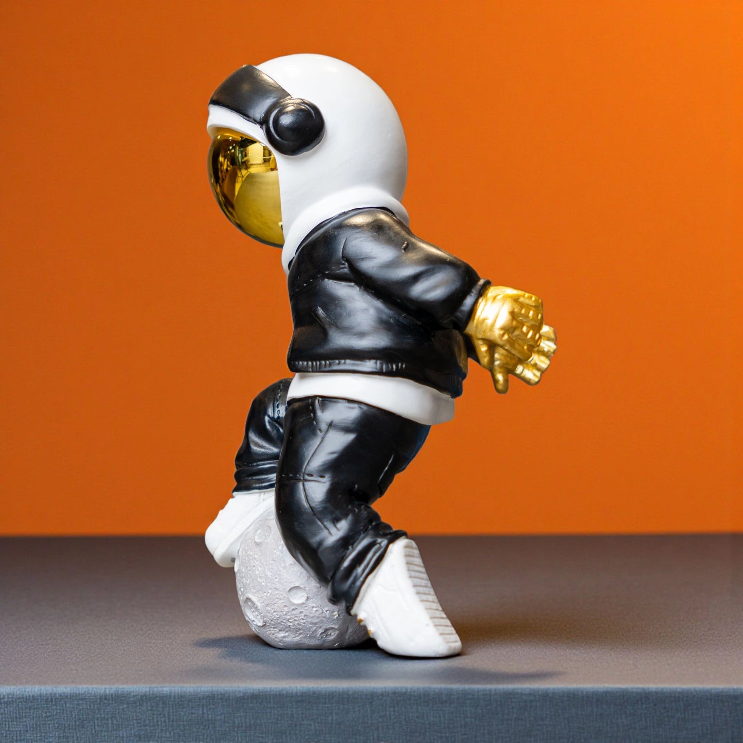 Resin astronaut figurine with gold visor in streetwear, leaning on a moon sphere — Cosmic Voyager by Ghar Art.
