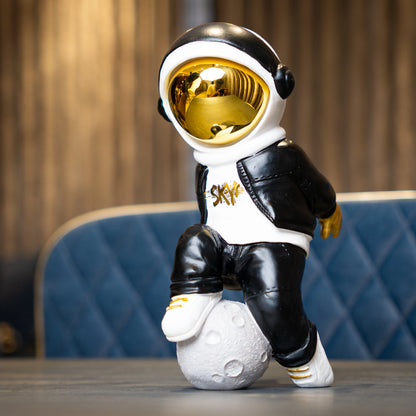 Resin astronaut figurine with gold visor in streetwear, leaning on a moon sphere — Cosmic Voyager by Ghar Art.