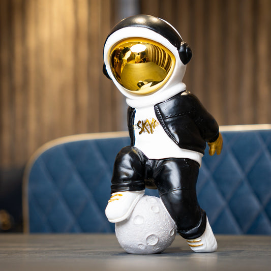 Resin astronaut figurine with gold visor in streetwear, leaning on a moon sphere — Cosmic Voyager by Ghar Art.