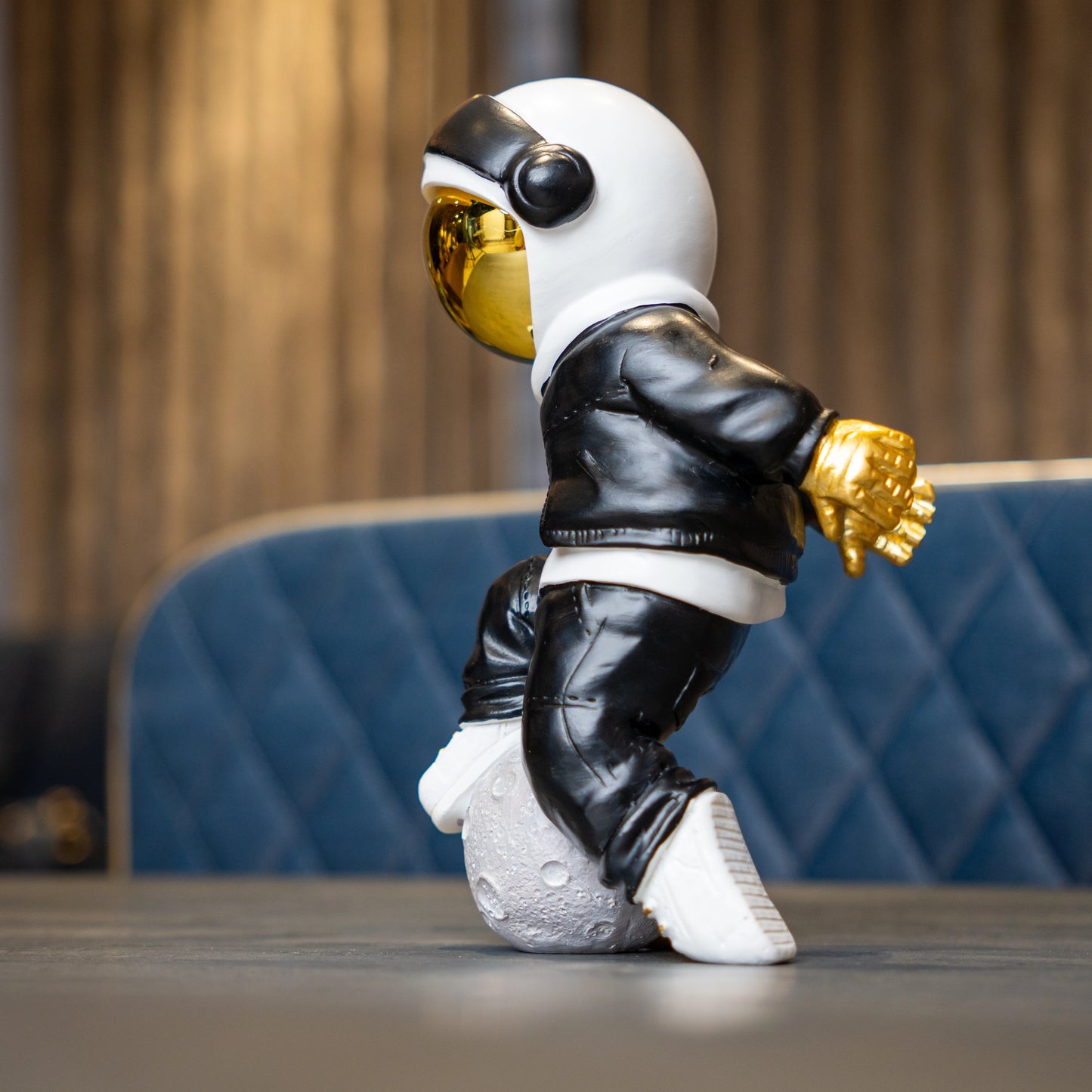 Resin astronaut figurine with gold visor in streetwear, leaning on a moon sphere — Cosmic Voyager by Ghar Art.