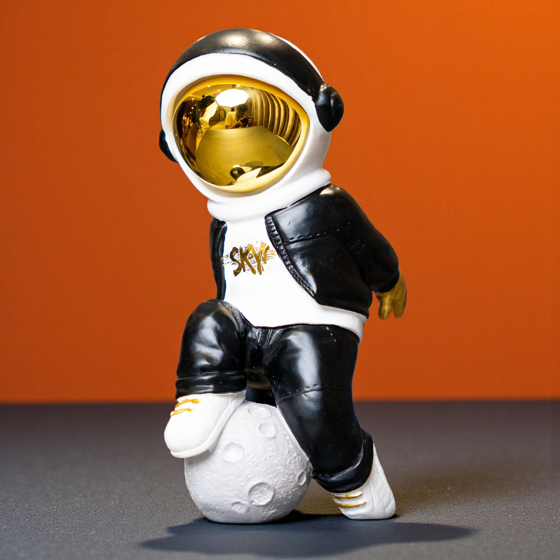Resin astronaut figurine with gold visor in streetwear, leaning on a moon sphere — Cosmic Voyager by Ghar Art.