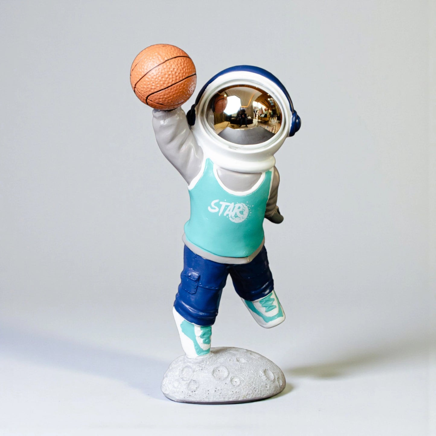 Astronaut figurine dribbling a basketball on a moon base with teal jersey and gold visor