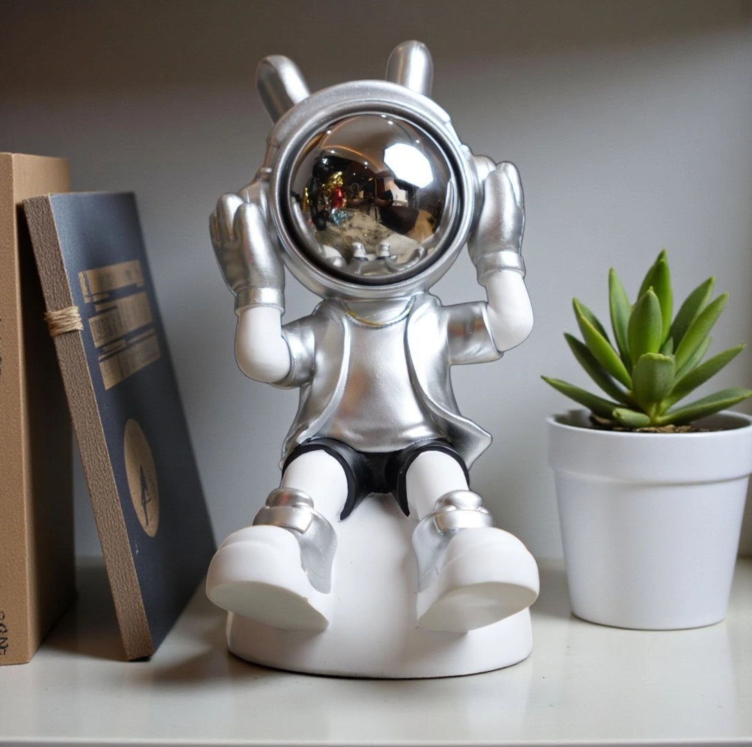 Seated silver and white astronaut figurine with headphones and chrome visor