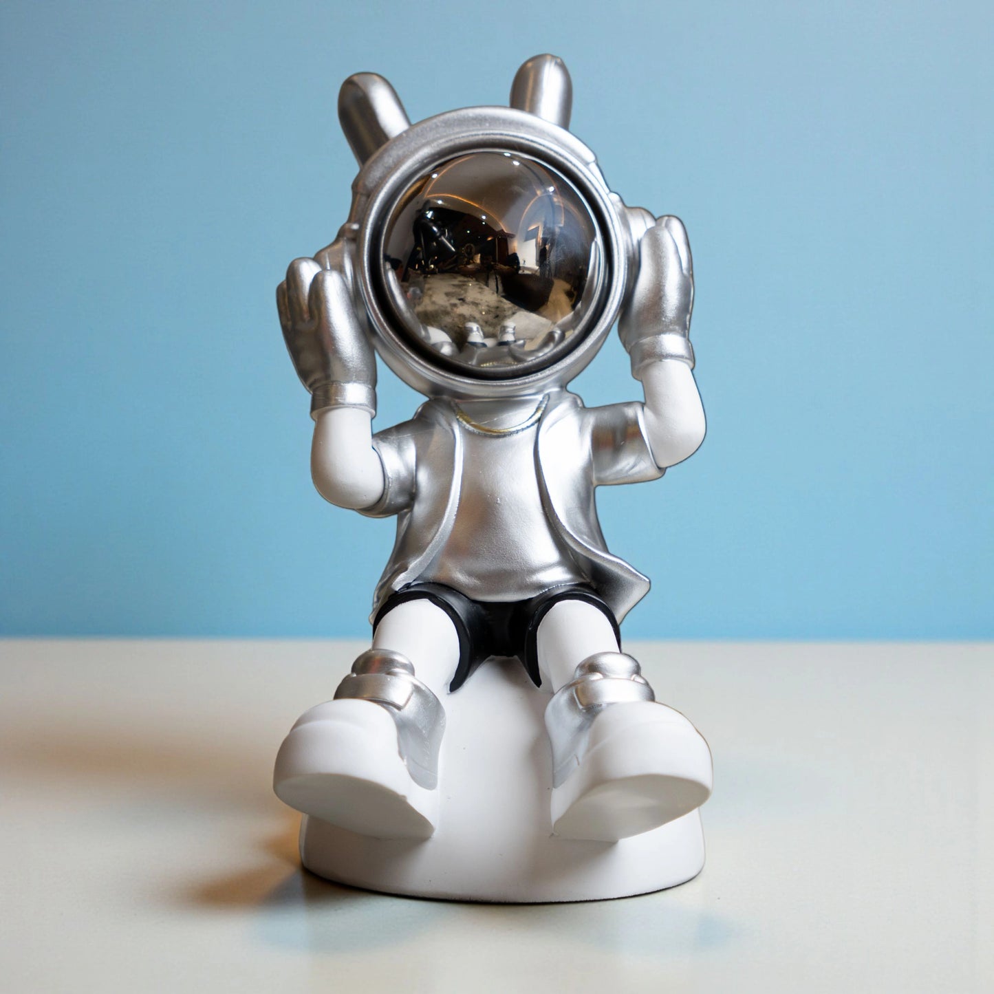 Seated silver and white astronaut figurine with headphones and chrome visor