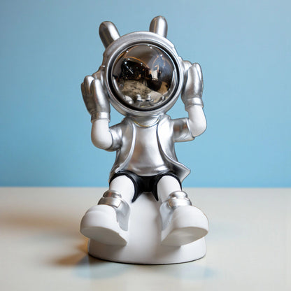 Seated silver and white astronaut figurine with headphones and chrome visor