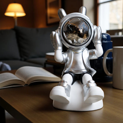 Seated silver and white astronaut figurine with headphones and chrome visor