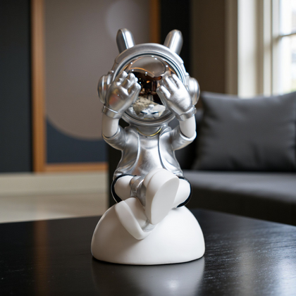 Seated astronaut figurine in silver suit covering chrome visor on white base