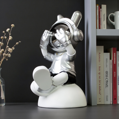 Seated astronaut figurine in silver suit covering chrome visor on white base