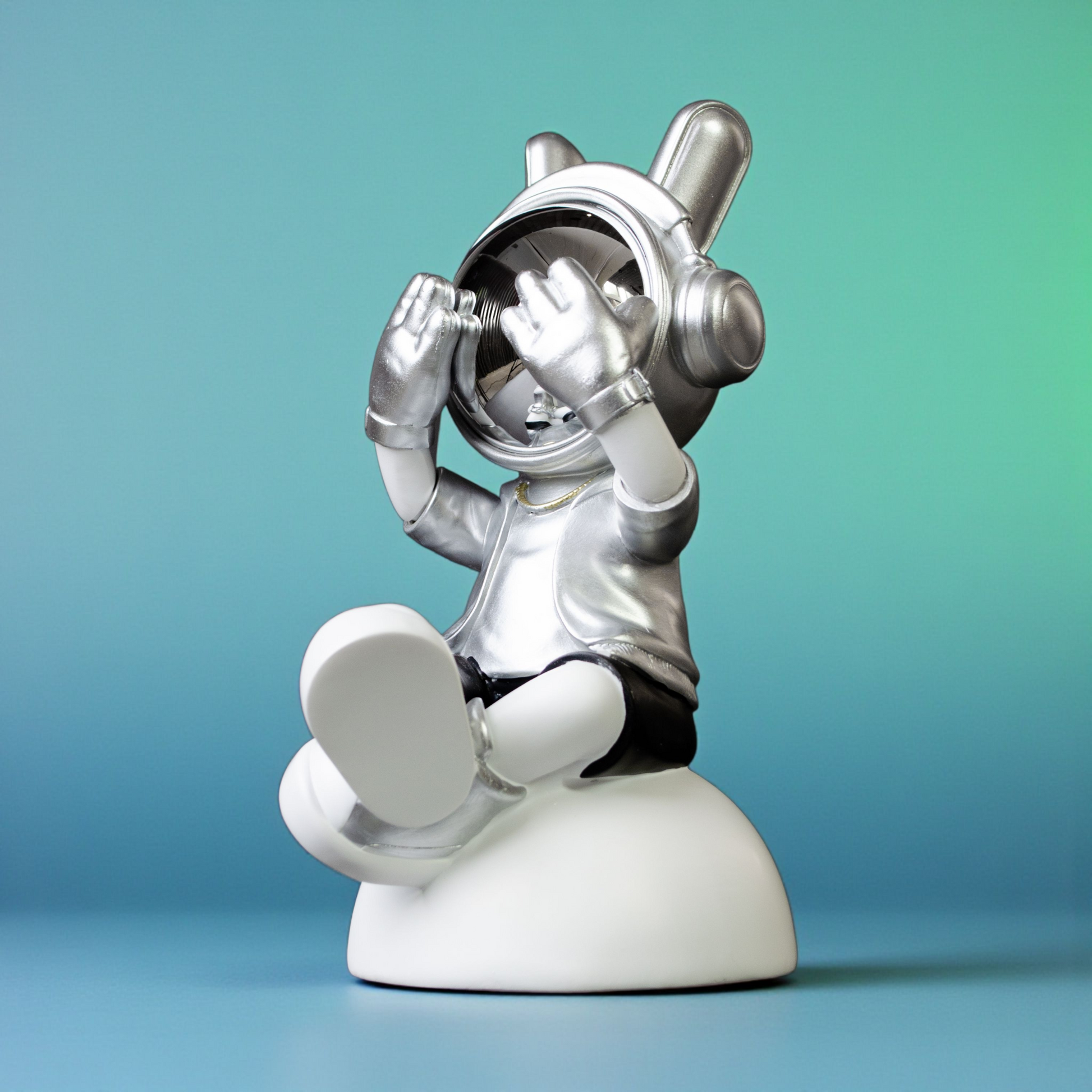 Seated astronaut figurine in silver suit covering chrome visor on white base