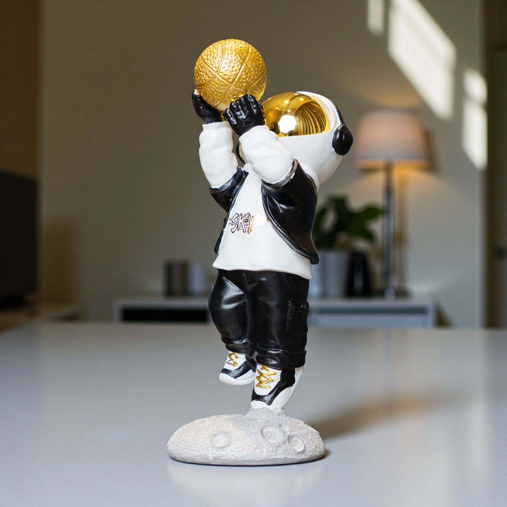 Astronaut figurine in black-and-white streetwear shooting a gold basketball on a moon base — Cosmic Shooter Figurine by Ghar Art.