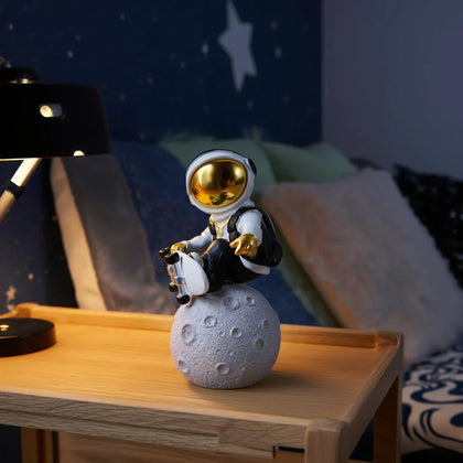 Small astronaut figurine on a moon-shaped object on a wooden surface with a lamp in the background.
