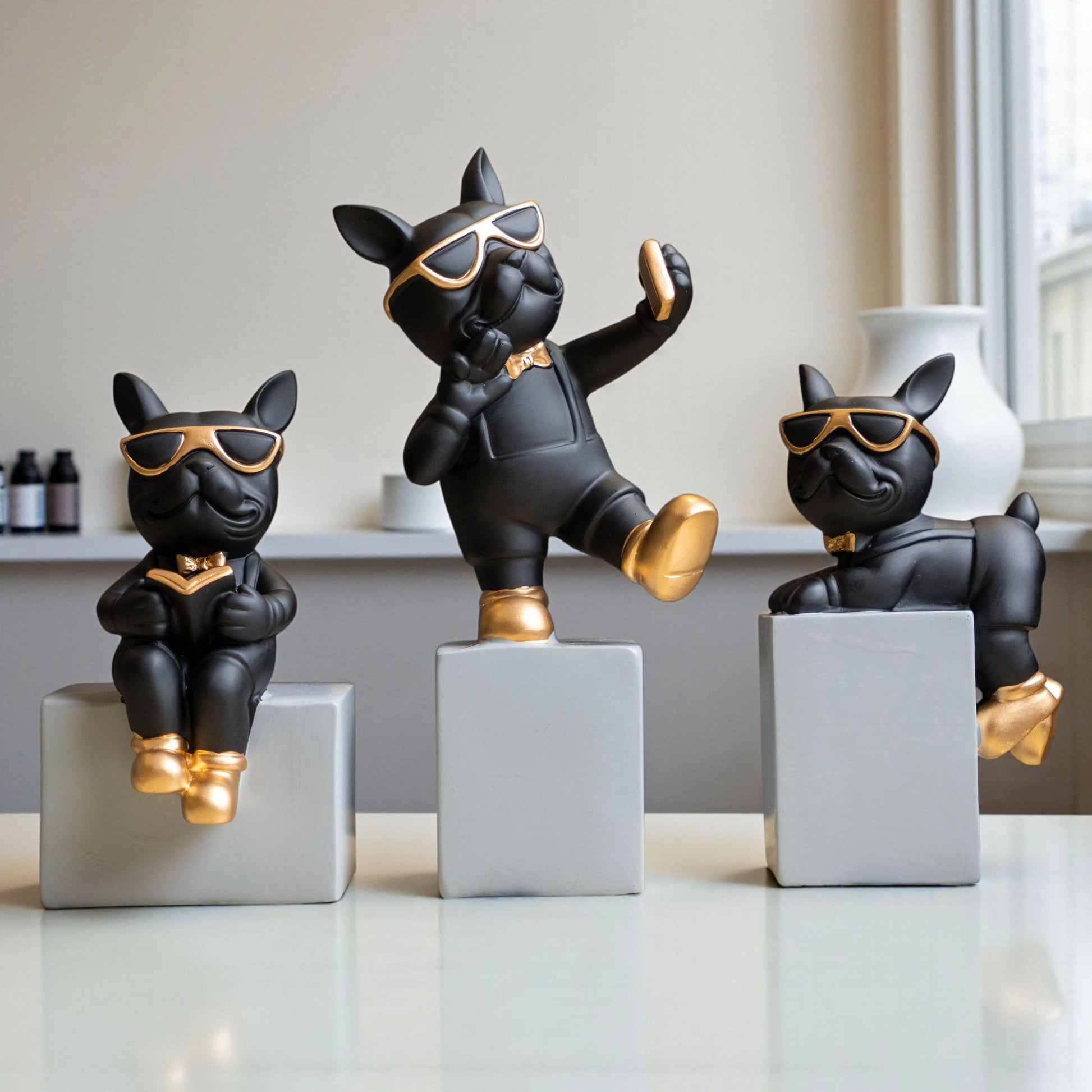 Black resin bulldog figurine trio with gold accents displayed on modern pedestal blocks