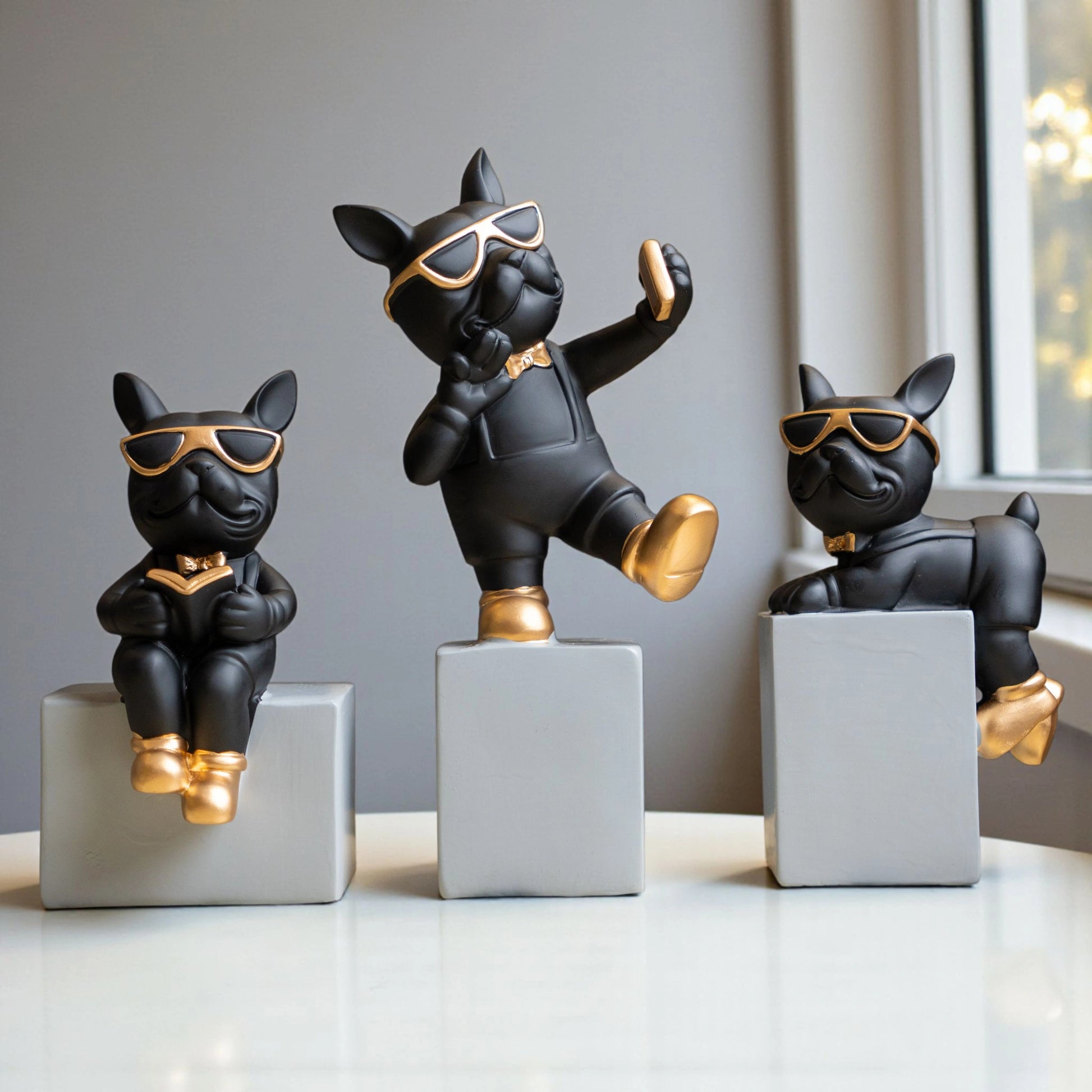 Black resin bulldog figurine trio with gold accents displayed on modern pedestal blocks