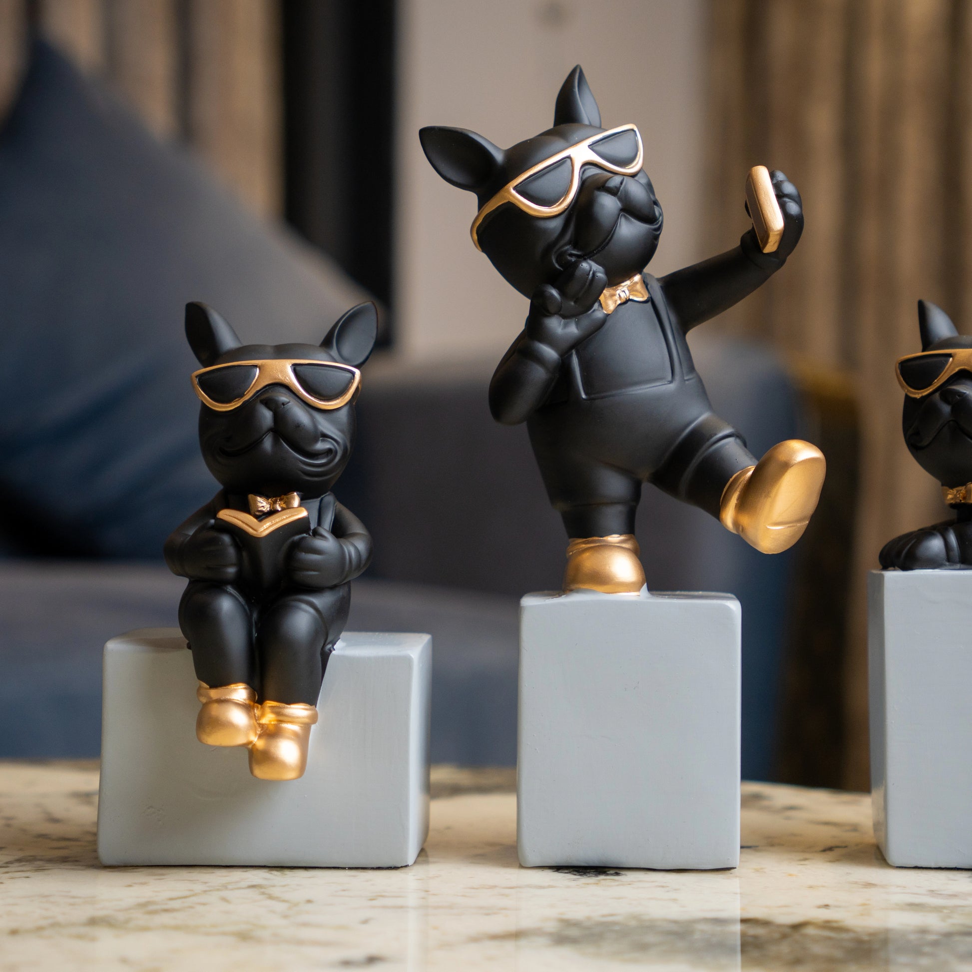 Black resin bulldog figurine trio with gold accents displayed on modern pedestal blocks