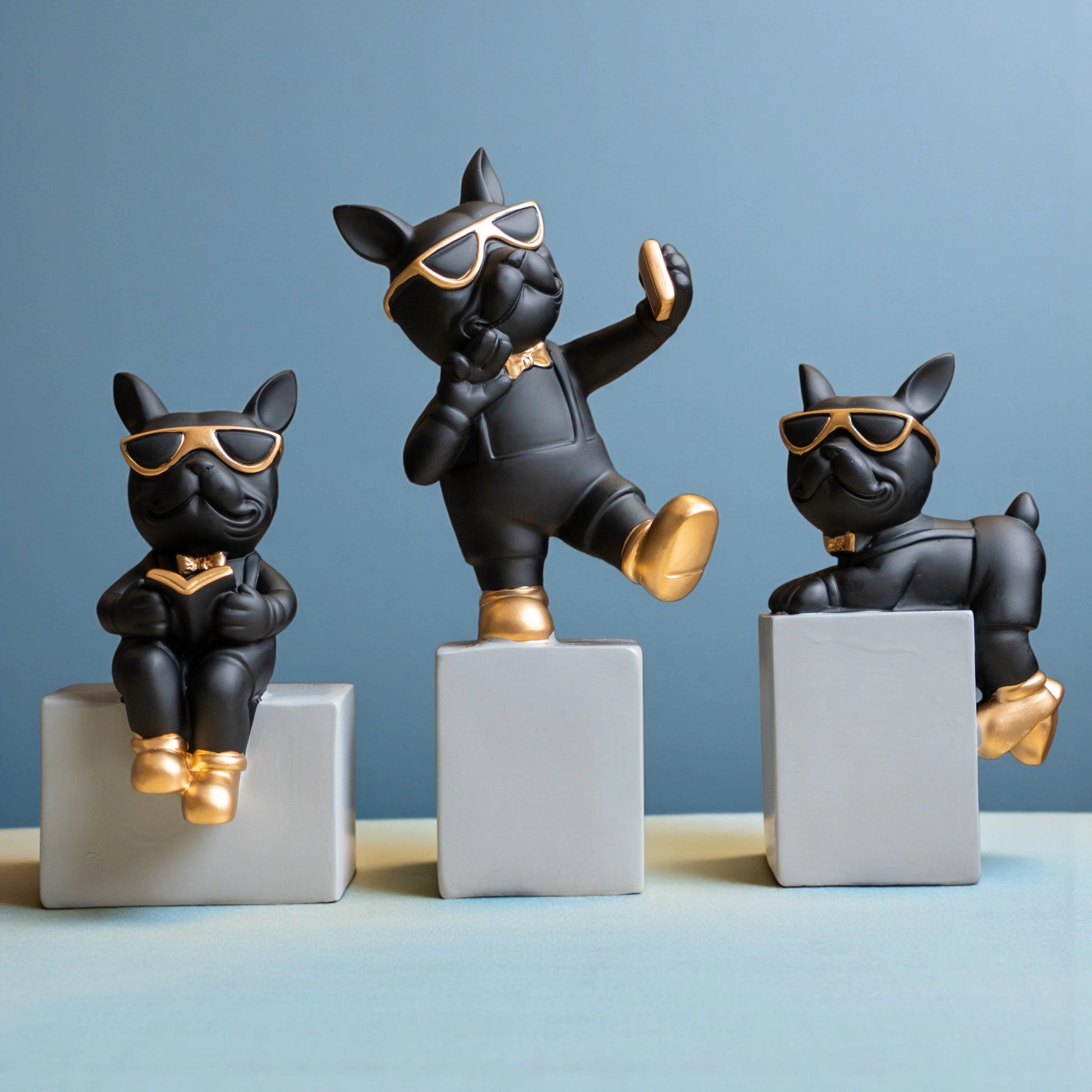 Black resin bulldog figurine trio with gold accents displayed on modern pedestal blocks