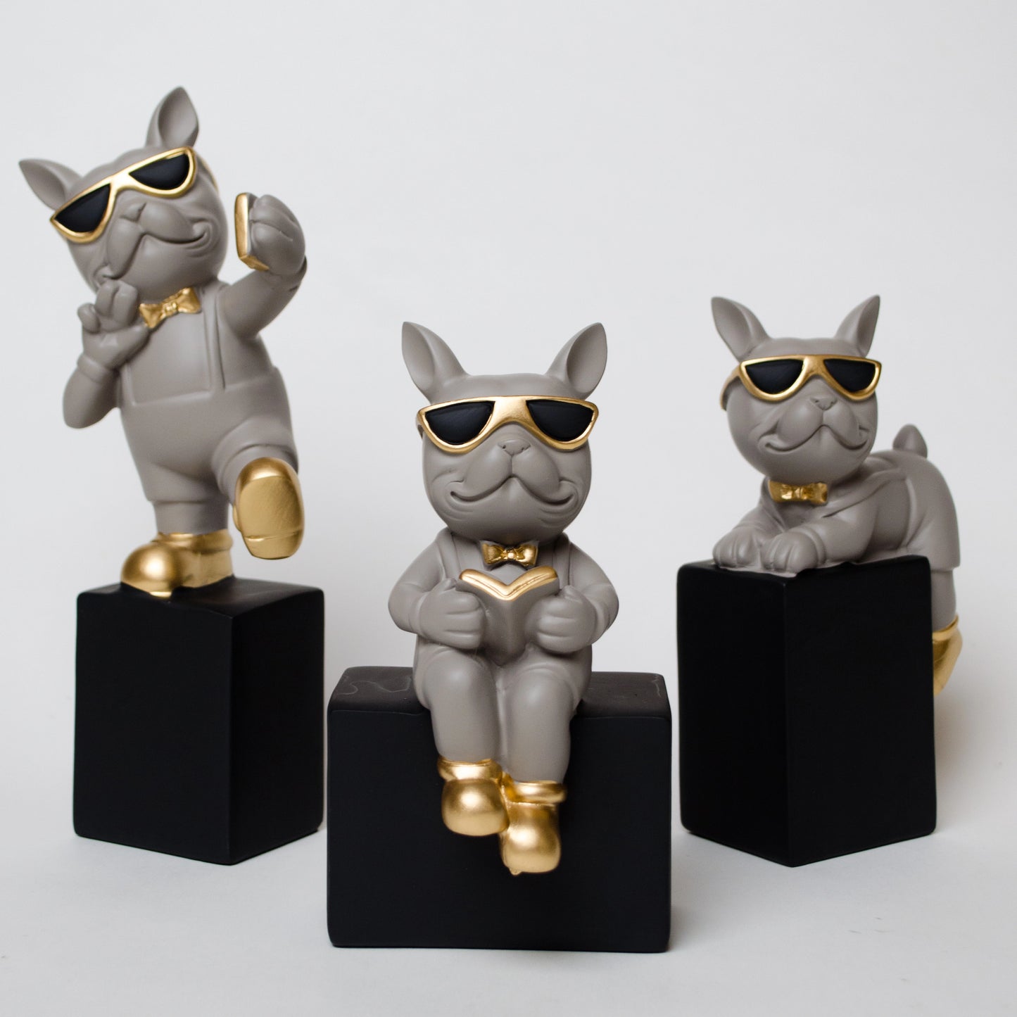 Grey resin bulldog figurine trio with gold accents displayed on black pedestal blocks