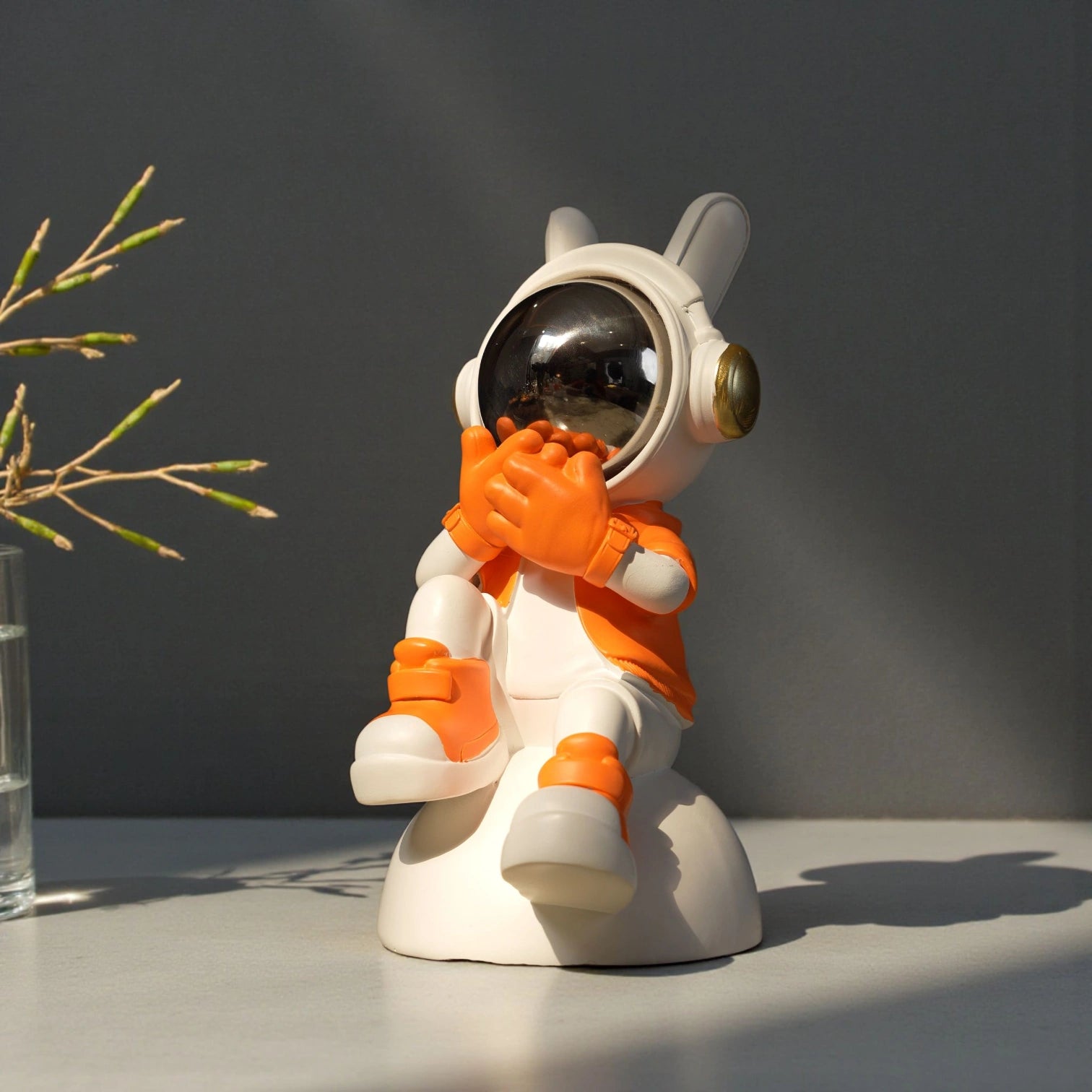 Astronaut whisper figurine in white and orange with chrome visor seated on a base—modern resin décor showpiece