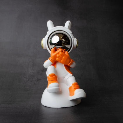 Astronaut whisper figurine in white and orange with chrome visor seated on a base—modern resin décor showpiece