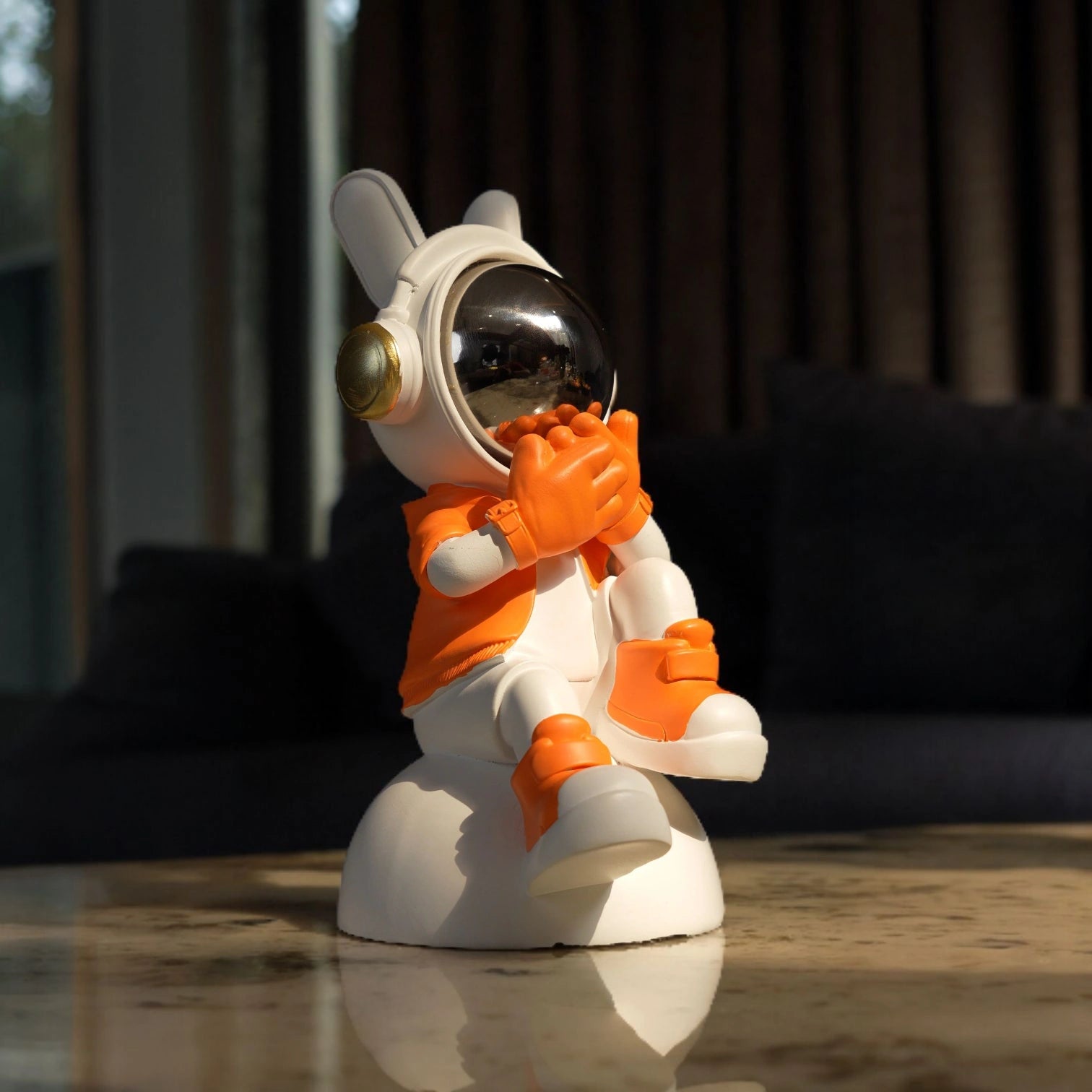 Astronaut whisper figurine in white and orange with chrome visor seated on a base—modern resin décor showpiece