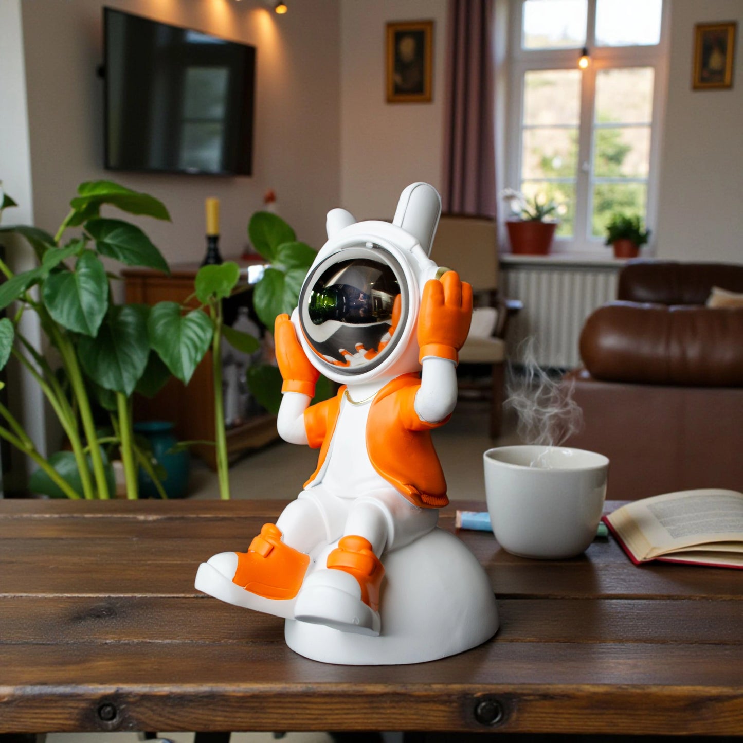 Astronaut figurine in orange and white holding its helmet sides in a listening pose with a chrome visor, seated on a dome-shaped base; modern resin décor piece