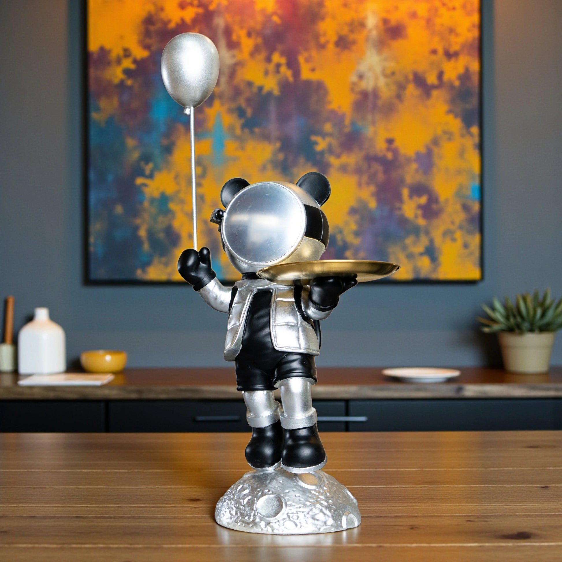 Astronaut bear figurine in silver and black holding a metallic balloon and a gold tray while standing on a moon-textured base; modern resin décor showpiece