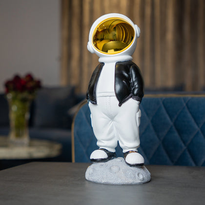 Astronaut figurine with gold visor, black jacket, white pants, and hands-in-pockets pose standing on a moon-textured base; modern resin décor showpiece