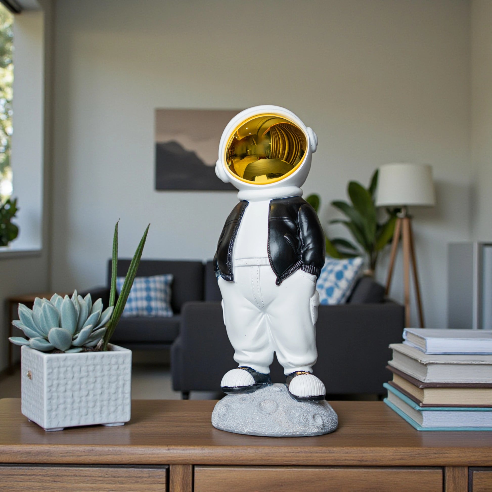 Astronaut figurine with gold visor, black jacket, white pants, and hands-in-pockets pose standing on a moon-textured base; modern resin décor showpiece