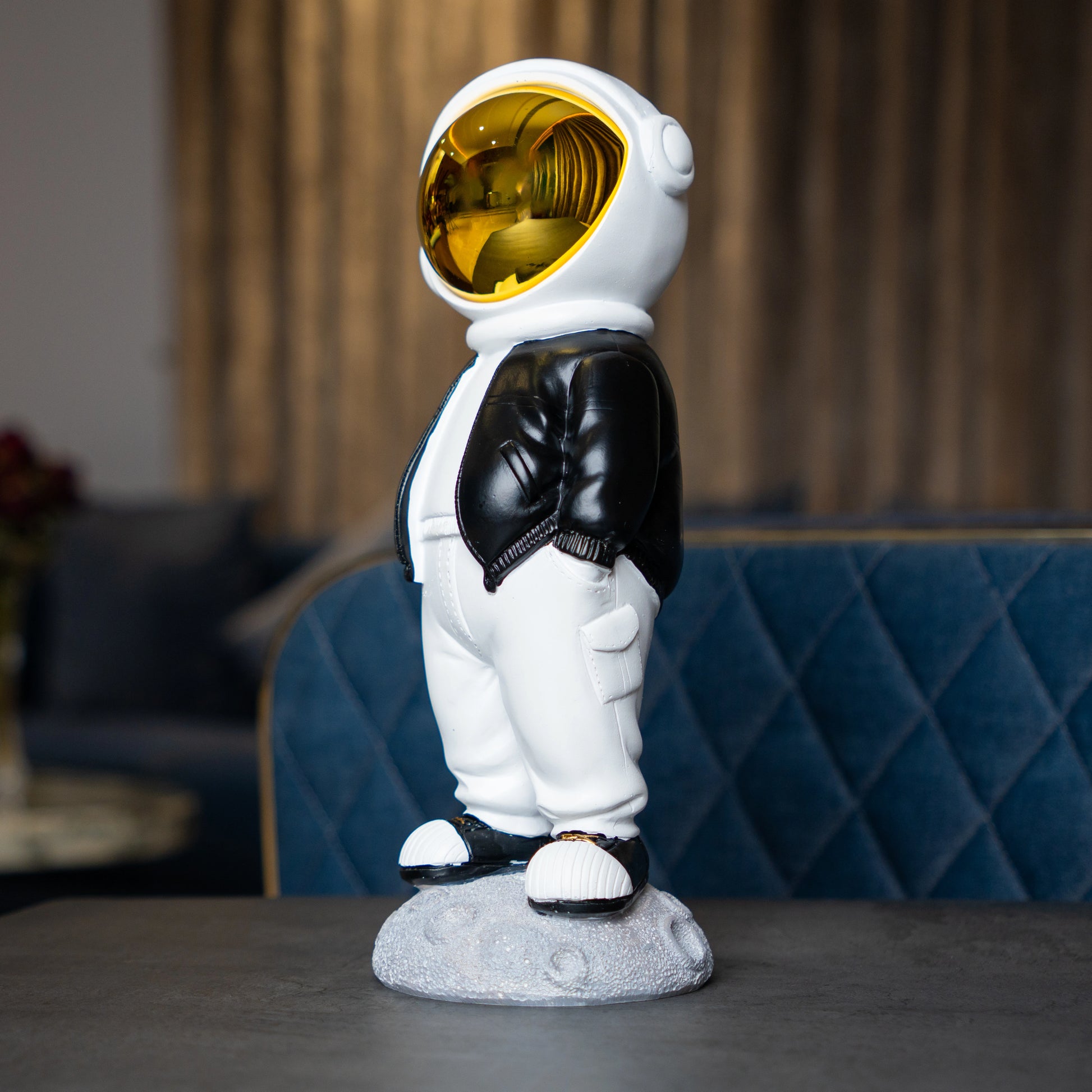 Astronaut figurine with gold visor, black jacket, white pants, and hands-in-pockets pose standing on a moon-textured base; modern resin décor showpiece