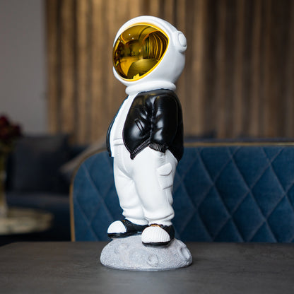 Astronaut figurine with gold visor, black jacket, white pants, and hands-in-pockets pose standing on a moon-textured base; modern resin décor showpiece