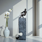 Bronze pulling figure sculpture on textured charcoal stone base with hanging weight.