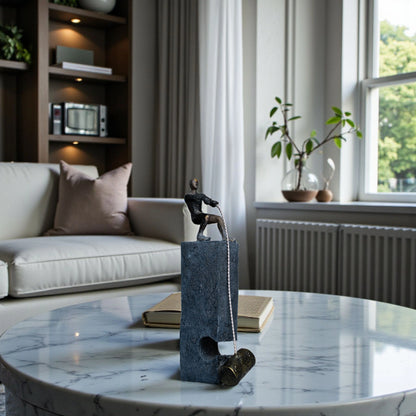 Bronze pulling figure sculpture on textured charcoal stone base with hanging weight.