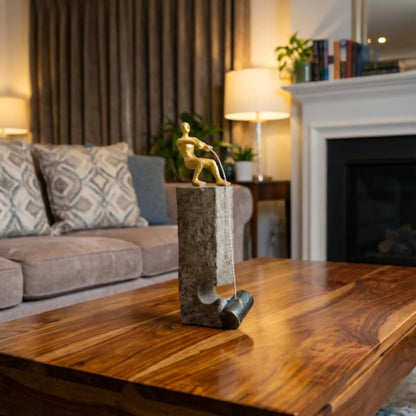 Gold pulling figure sculpture on textured charcoal stone base with hanging weight.