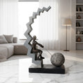 Abstract human figure decor seated on geometric staircase holding chain with sphere, modern tabletop accent for living room, office desk or console styling