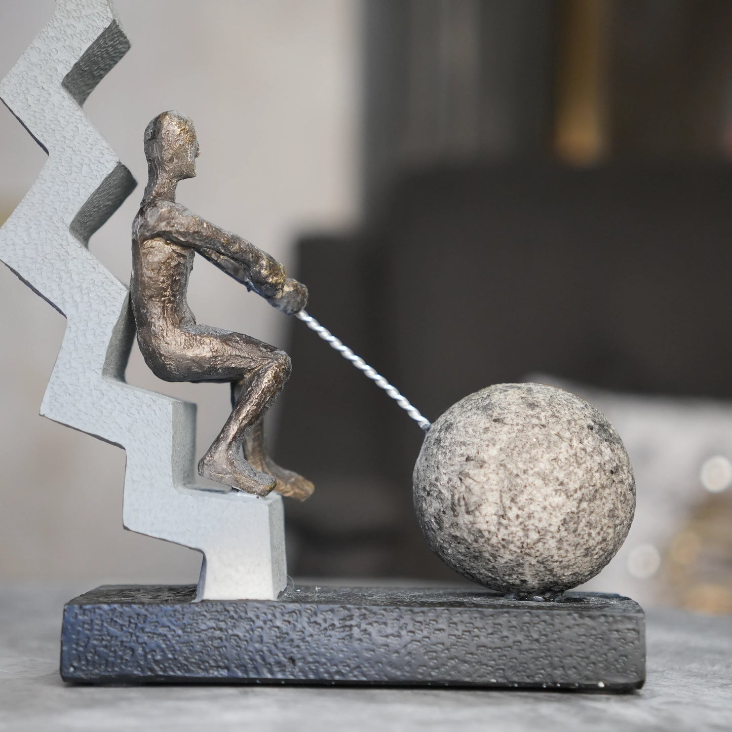 bronze figure pulling sphere on textured steps sculpture