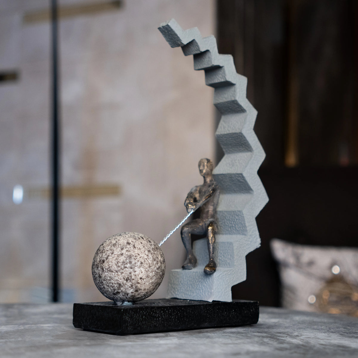 Abstract human figure decor seated on geometric staircase holding chain with sphere, modern tabletop accent for living room, office desk or console styling