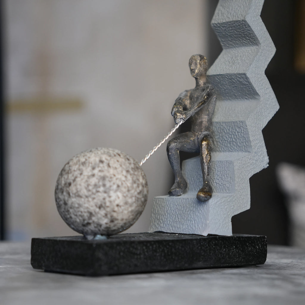 bronze figure pulling sphere on textured steps sculpture