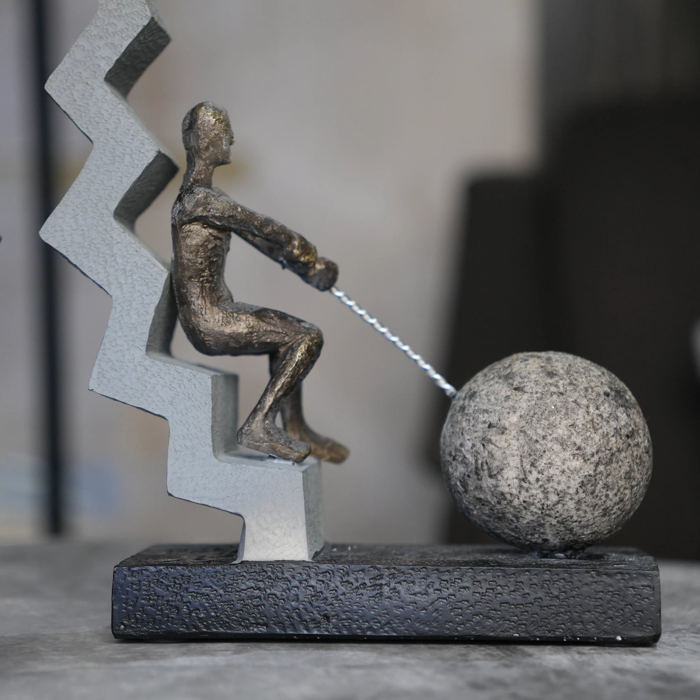 bronze figure pulling sphere on textured steps sculpture