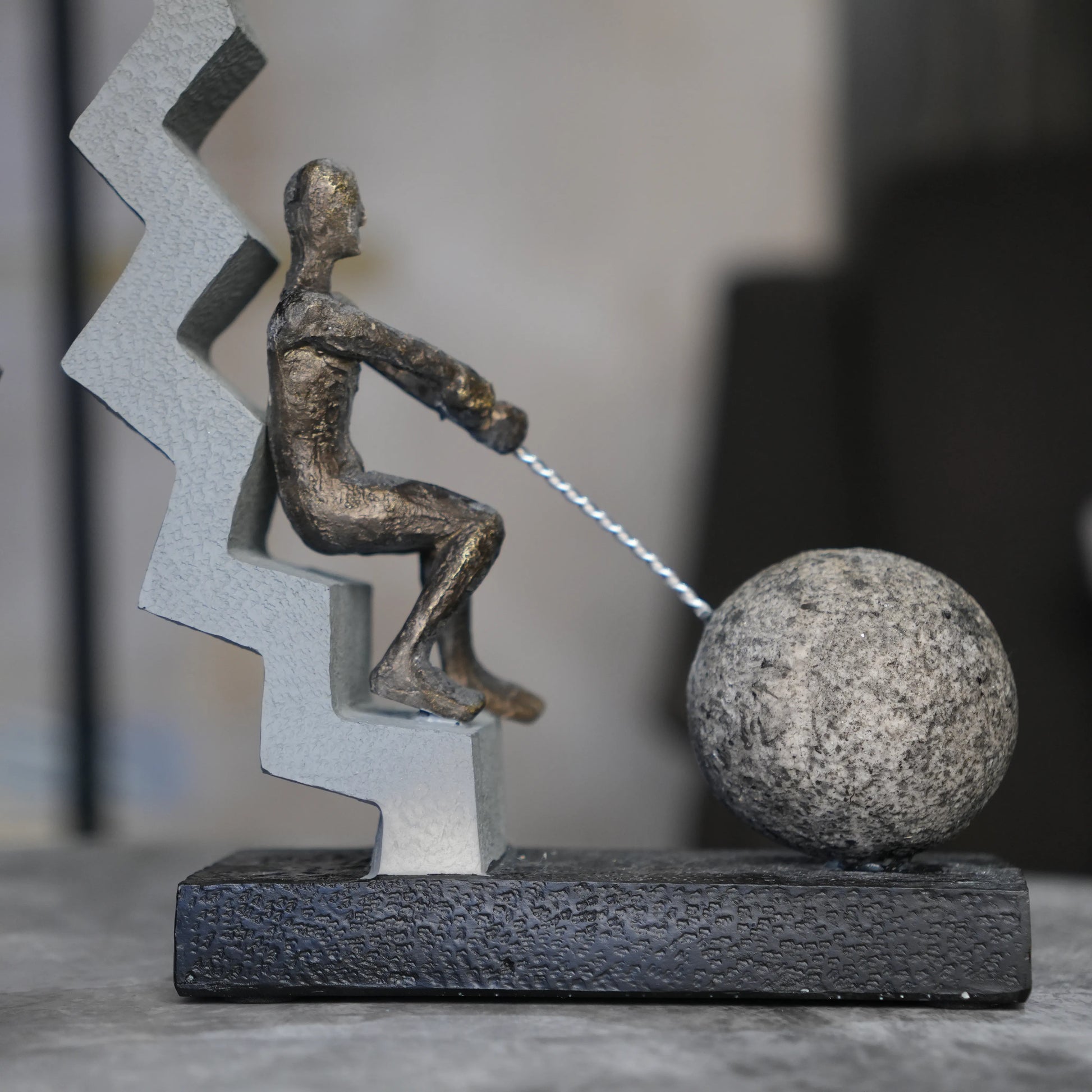 bronze figure pulling sphere on textured steps sculpture