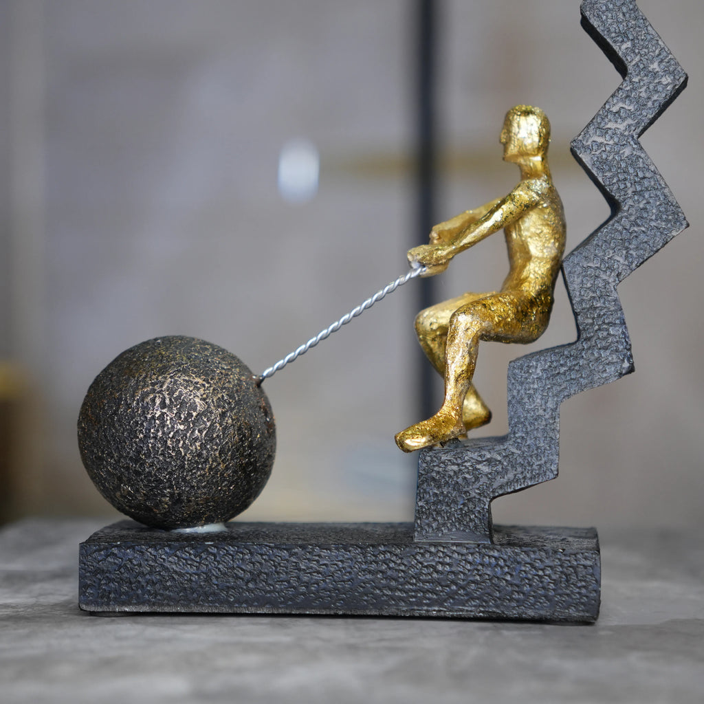 gold figure pulling sphere on textured steps sculpture