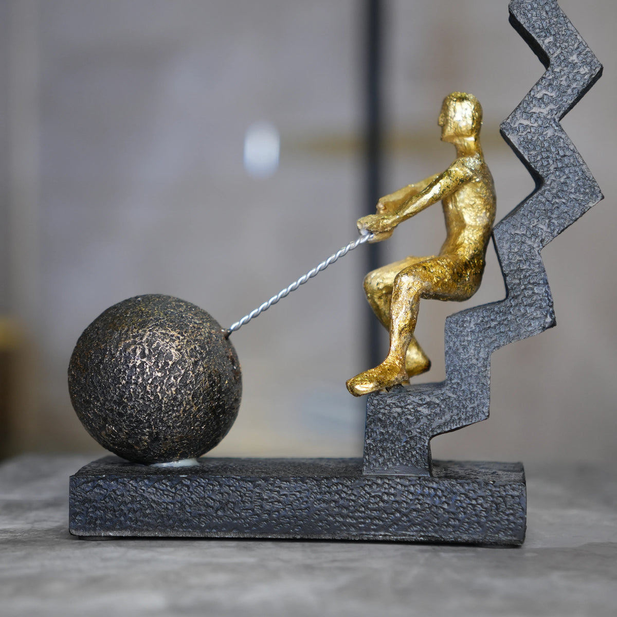 gold figure pulling sphere on textured steps sculpture