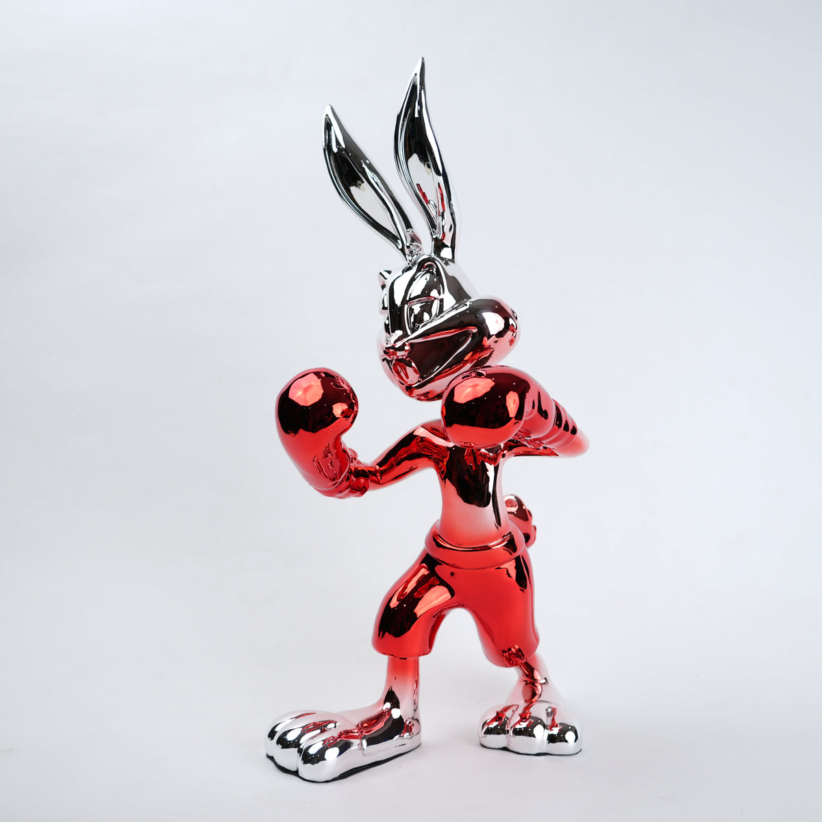 A glossy, highly reflective metallic sculpture of a cartoon rabbit character in a boxing pose, finished in a vibrant red with silver chrome accents, set against a plain light gray background.