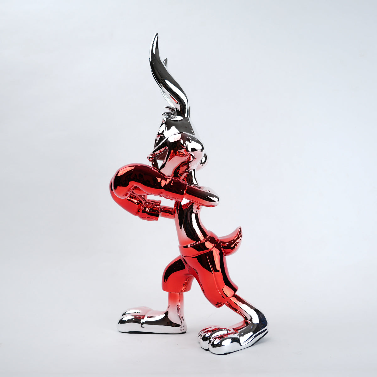 A glossy, metallic red and silver sculpture of a cartoon rabbit character, posed in a dynamic crouching stance against a clean, light gray studio background.