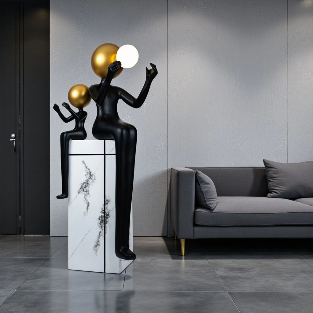 Black and gold human figurine duo holding a glowing orb on a marble pedestal sculpture
