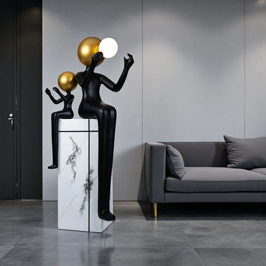 Black and gold human figurine duo holding a glowing orb on a marble pedestal sculpture