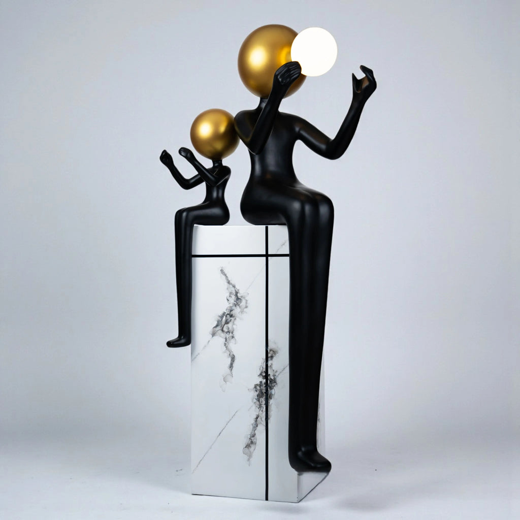 Black and gold human figurine duo holding a glowing orb on a marble pedestal sculpture